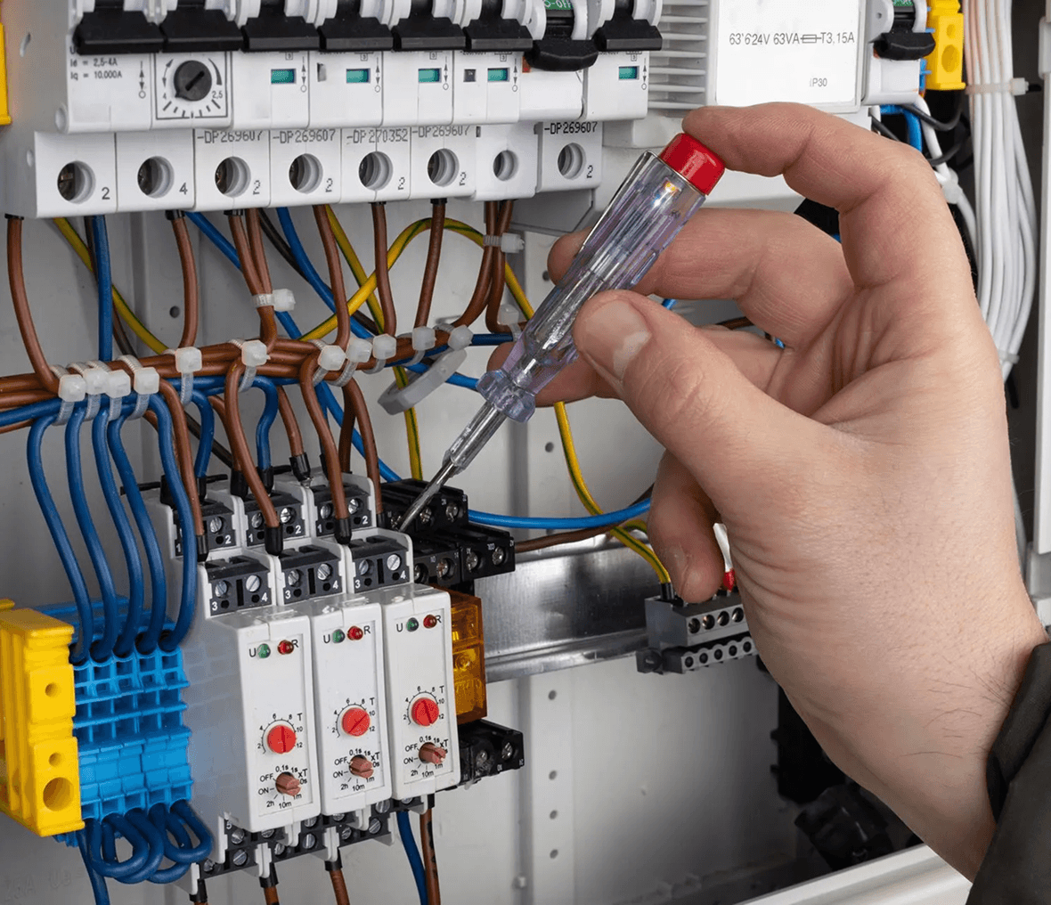 Hand adjusting electrical components with screwdriver.