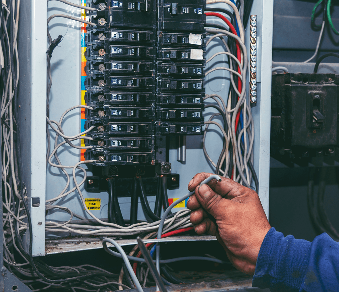 Hand working on electrical circuit breaker panel.